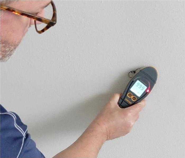 moisture meter held by a SERVPRO technician, hand on frame holding a small remote-looking device with screen,